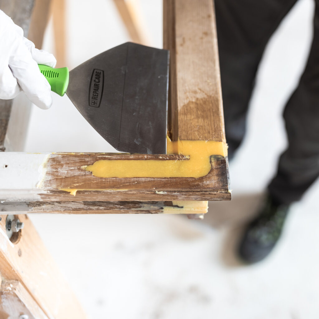 Ein Repair Care Anwender spachtelt eine mit DRY FLEX® Holzreparaturmasse gefüllte Reparaturstelle ab.