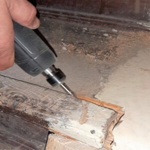 Ein Handwerker fräst entstandene Risse in einer Holztreppe aus, um die beschädigten Stellen fachgerecht zu reparieren.